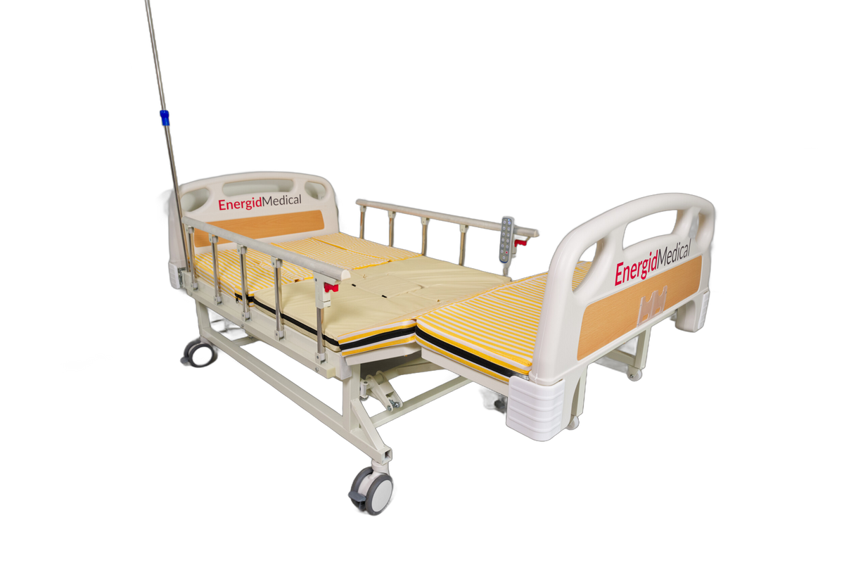 An EnergyMedica L4 adjustable hospital bed with a beige mattress, side rails, and an attached IV pole, shown on a solid white background.